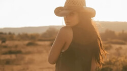 Woman wearing a cowboy hat standing in an arid desert landscape during golden hour.