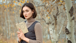 Woman holding an open book in an autumn forest with birch trees.