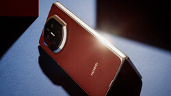 Red smartphone with metallic frame and large camera module, positioned at an angle on a light surface with dramatic directional lighting.