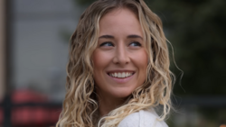 Young woman with wavy blonde hair smiling at camera outdoors.