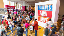 Crowded convention center floor with attendees walking past illuminated signage reading "CONNECT LEARN THRIVE."