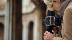 Photographer holding a large format film camera with telephoto lens in an urban alleyway.