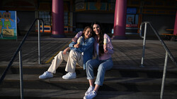 Three young people sitting together on a shaded platform with colorful building columns in background.