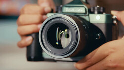 Photographer's hands holding a vintage SLR camera with lens extended, demonstrating proper grip and positioning.