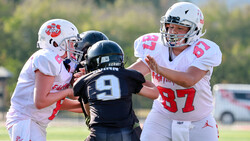 Youth football players in white and black uniforms competing for the ball during a daytime game.