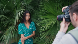 Portrait photographer shooting a woman posed against lush green palm fronds.