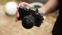 Hand holding a Fujifilm X-T30 mirrorless camera with attached lens outdoors.
