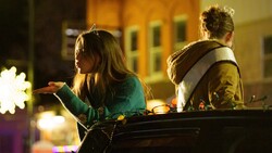 Two people sitting outdoors at night, illuminated by warm ambient lighting and decorative lights in the background.