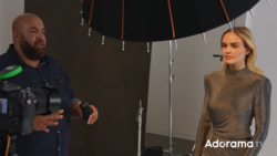 Cinematographer operating camera while interviewing woman under large softbox lighting setup.