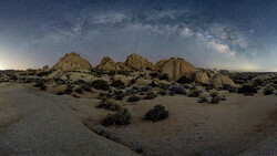Desert landscape with large granite rock formations under a starry night sky with visible Milky Way.