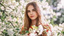Woman with long brown hair surrounded by blooming white flowers in natural outdoor light.