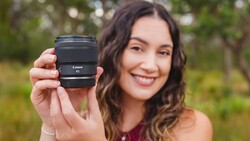 Woman holding a Canon RF mount lens toward the camera in an outdoor garden setting.
