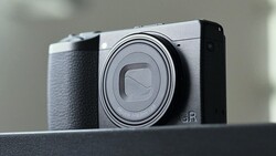 Ricoh GR compact camera with silver top plate and black grip, shown in three-quarter view against neutral background.