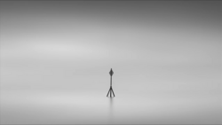 Solitary communication tower standing in fog with minimal ground visibility.