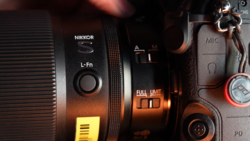 Nikon L-Fn lens with camera body and accessories in warm studio lighting.