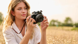 Woman holding a black film camera while standing in an open field during golden hour.