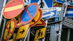 Stacked traffic signs with red no-entry circles and yellow warning signs featuring pedestrian symbols.