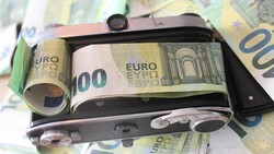 Vintage film camera wrapped in Euro banknotes, photographed on a surface covered with additional currency.