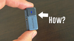 Close-up of a small blue portable audio device held between two fingers, with a white arrow pointing to the top surface and text reading 'How?'.