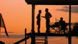 Silhouetted figures on a waterfront deck during golden hour sunset.