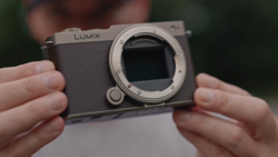 Panasonic Lumix mirrorless camera body held in hands, showing open sensor mount and textured grip.