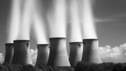 Cooling towers of an industrial power plant emitting white steam plumes against a dramatic sky in black and white.