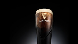 A pint glass of Guinness with a thick cream-colored head against a dark background.
