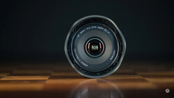 Camera lens viewed head-on against a dark background, positioned on a reflective wooden surface.