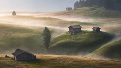 Alpine valley at sunrise with scattered wooden chalets nestled on misty hillsides surrounded by evergreen forests.