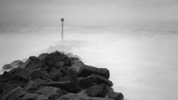 A communications tower rises from a rocky summit shrouded in mist and clouds.