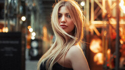 Woman with long blonde hair looking over shoulder in urban evening setting with warm golden lighting.