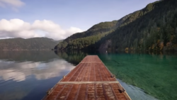 Wooden dock extending into a turquoise alpine lake surrounded by forested mountains.