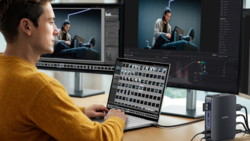 Video editor working at dual monitors with control panel and editing software open.