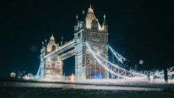 Tower Bridge in London illuminated at night with atmospheric mist surrounding its base.