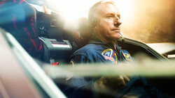 Pilot wearing headset in aircraft cockpit, backlit by golden sunlight streaming through windows.