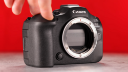 Canon EOS R6 Mark II mirrorless camera body held against red background, showing open mount without lens.