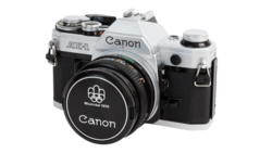 Canon AE-1 35mm SLR camera with silver top plate and black body, shown with standard lens and lens cap.