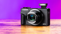 Canon PowerShot G7 X compact camera on reflective surface against vibrant magenta and gold gradient backdrop.