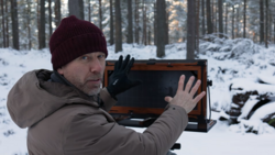Photographer holding a large format camera in snowy forest setting.