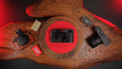 Rangefinder camera with lens and accessories arranged on carved wooden surface.