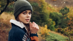 Woman in gray beanie and dark jacket with sherpa collar looking over shoulder outdoors.