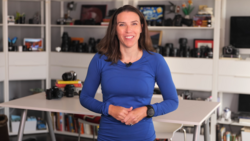 Woman in blue long-sleeve shirt standing in front of white shelving unit filled with camera equipment.