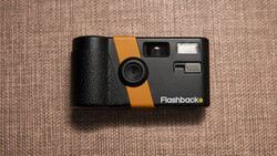 Flashback vintage film camera with black body and orange stripe on beige fabric background.