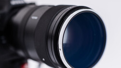 Close-up of a telephoto lens with a dark blue circular filter element and metallic focus ring against a white background.