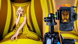 Studio setup with female model in yellow dress against striped backdrop, professional video camera on tripod in foreground.