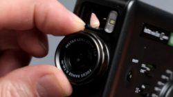 Hand holding a Fujifilm Instax instant camera with lens visible and flash unit mounted on top.