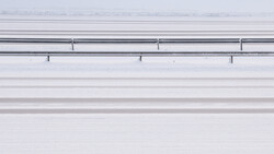 Aerial view of a snow-covered highway with guardrails and lane markings visible from above.