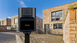 Electric vehicle charging station mounted on pole in residential street with brick buildings.