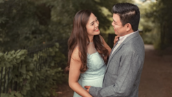 Couple embracing outdoors among green foliage in soft natural light.