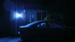 Parked sedan covered in snow beneath a blue-tinted streetlight at night.